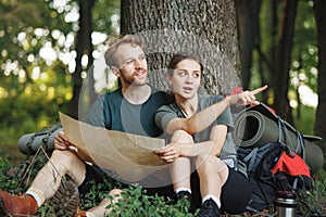 Photo of couple sitting in forest at summer with backpacks