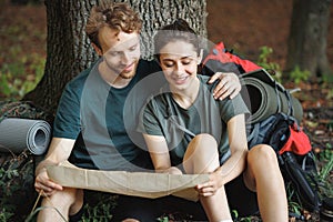 Photo of couple sitting in forest at summer with backpacks