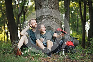 Photo of couple sitting in forest at summer with backpacks