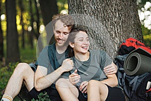 Photo of couple sitting in forest at summer with backpacks