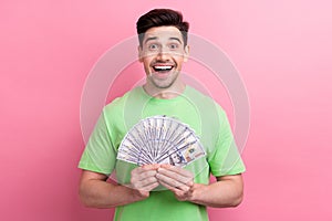 Photo of crazy business startuper guy wearing green t shirt holding banknotes received big investments isolated on pink
