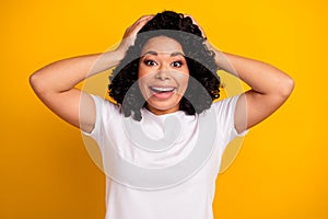 Photo of crazy overjoyed ecstatic woman dressed white t-shirt hold arms on head astonished staring isolated on yellow