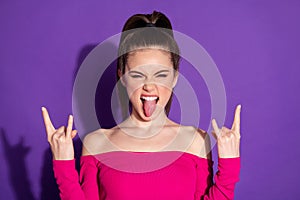 Photo of crazy young girl raise two arms show horns stick out tongue wear pink uncovered shoulders top isolated violet