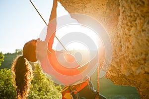 Photo of curly-haired female tourist clambering over rock