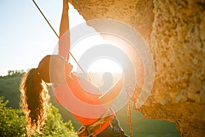 Photo of curly-haired female tourist clambering over rock