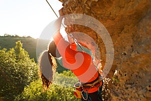 Photo of curly-haired female tourist clambering over rock