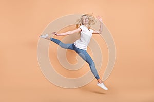 Photo of cute adorable young woman dressed white t-shirt jumping high walking waving arm smiling isolated beige color