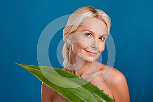 Photo of cute charming senior woman nude shoulders smiling enjoying handmade natural aloe cosmetics isolated blue color