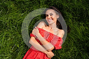 Photo of cute charming young lady wear red off-shoulders dress resting green grass embracing herself outside countryside