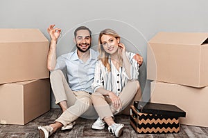 Photo of cute couple in casual clothing seating near cardboard boxes and holding flat keys