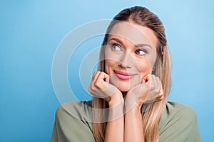 Photo of cute dreamy young woman dressed green clothes arms cheeks chin looking empty space smiling isolated blue color