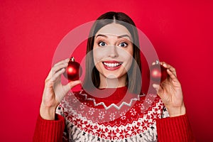 Photo of cute funny young lady wear print sweater holding chrismas balls smiling isolated red color background