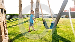 Image of cute little toddler boy playing with swings on the palyground at park photo