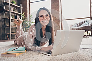 Photo of cute optimistic girl lying write laptop wear spectacles pijama at home