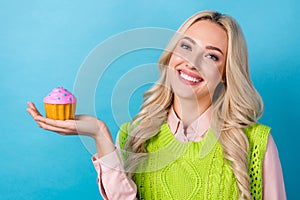 Photo of cute positive girl toothy smile arm palm hold small cupcake isolated on blue color background
