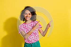 Photo of cute positive girl toothy smile indicate fingers empty space ad blank isolated on beige color background