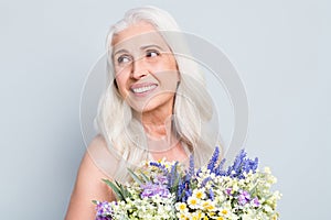 Photo of cute retired woman beaming smile hold big bunch wild flowers look empty space shy isolated grey color