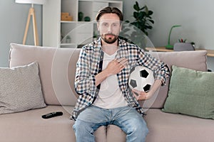 Photo of cute serious guy dressed checkered shirt sitting couch watching football match listening anthem indoors