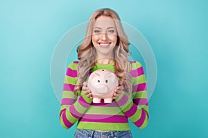 Photo of cute sweet woman dressed striped sweater holding pig money box smiling isolated turquoise color background