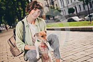 Photo of cute sweet young woman wear green shirt rucksack smiling walking holding little pappy outside city street