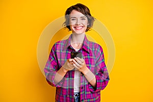 Photo of cute trendy happy girl wear plaid shirt hold phone good sms isolated on yellow color background