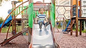 Photo of cute 3 years old toddler boy climbing and riding on big slide on children playground at park