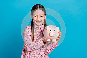 Photo of cute young funny schoolgirl kid brunette hold piggy bank collect money cash savings for dream  on blue