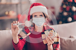 Photo of cute young ill girl hold many packs meds thermometer wear mask santa cap red pullover decorated living room