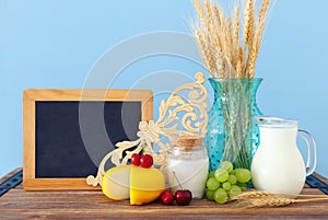 Photo of dairy products over old wooden table and pastel background. Symbols of jewish holiday - Shavuot