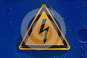 Photo of Danger High Voltage Sign on painted blue metal door. Outdoor Shot of High Voltage symbol on a sunny day.