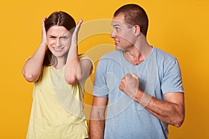 Photo of dangerous angry man holding fist, going to make pain for his girlfriend, looking at her with dissatisfaction, nervous
