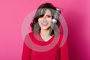 Photo of dark haired girl combs her hair, has some problems, hairbrush tangled in curls, stands smiling against rose wall, wears