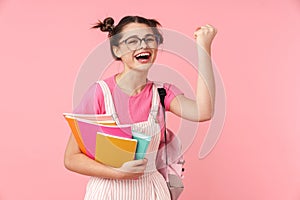 Photo of delighted girl holding exercise books and making winner gesture