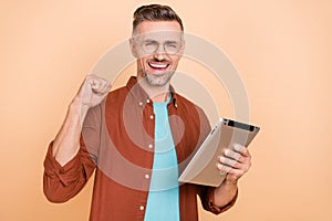 Photo of delighted middle-aged guy use gadget application raise fists up shopping sale isolated over pastel beige color