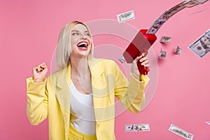 Photo of delighted successful girl raise fist hold money gun shoot dollar bills isolated on pink color background