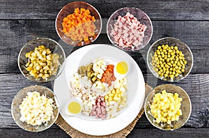 Ingredients shredded for salad in transparent plates on a black wooden background. Olives, pickled cuc