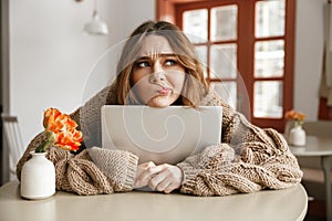Photo of disappointed woman in sweater looking aside with suspicious gaze, while hugging laptop in coffee shop photo