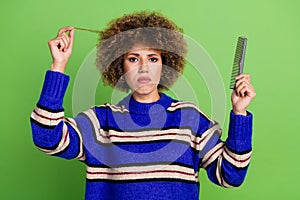 Photo of dissatisfied woman with perming coiffure wear knit sweater holding frizz in fingers comb isolated on green photo