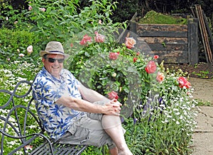 Gentleman in garden wearing summer panama trilby hat flowers roses seat bench