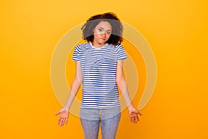 Photo of doubtful funny girl dressed striped t-shirt shrugging shoulders isolated yellow color background