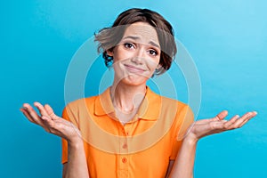 Photo of doubtful unsure girl dressed orange polo shrugging shoulders isolated blue color background