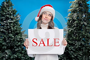 Photo of doubtful unsure girl dressed santa claus helper hat selling x-mas firs looking empty space isolated blue color