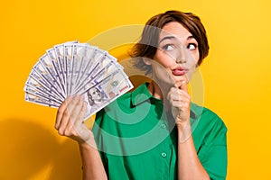 Photo of doubtful unsure lady wear green shirt arm chin looking money fan empty space isolated yellow color background