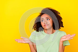 Photo of doubtful unsure lady wear green t-shirt shrugging shoulders looking empty space isolated yellow color