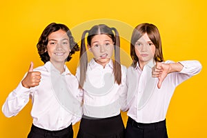 Photo of doubtful unsure schoolkids formalwear rising showing thumb up thumb down isolated yellow color background