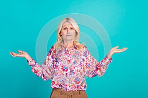 Photo of doubtful unsure woman dressed print shirt shrugging shoulders comparing empty space isolated turquoise color