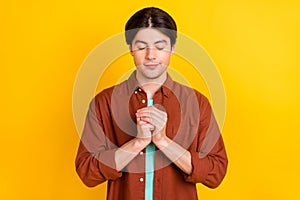 Photo of dreamy charming young man wear brown shirt arms together closed eyes praying isolated yellow color background