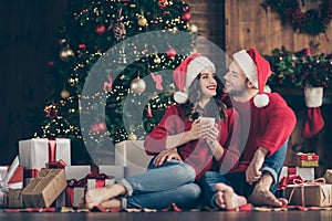 Photo of dreamy couple newyear night in decorated garland lights room sitting cozy on floor near x-mas tree drinking hot