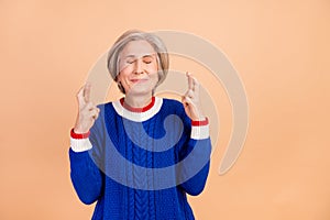 Photo of dreamy cute pensioner with closed eyes crossed wingers waiting miracle empty space isolated on beige color