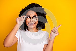 Photo of dreamy cute woman wear white t-shirt arm spectacles looking showing finger empty space isolated yellow color